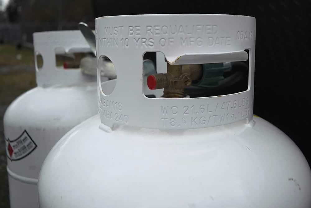 Close-up of two white propane tanks with a focus on the valve and stamped text indicating requalification requirements and manufacturing date, highlighting the essentials for safe Propane Services.