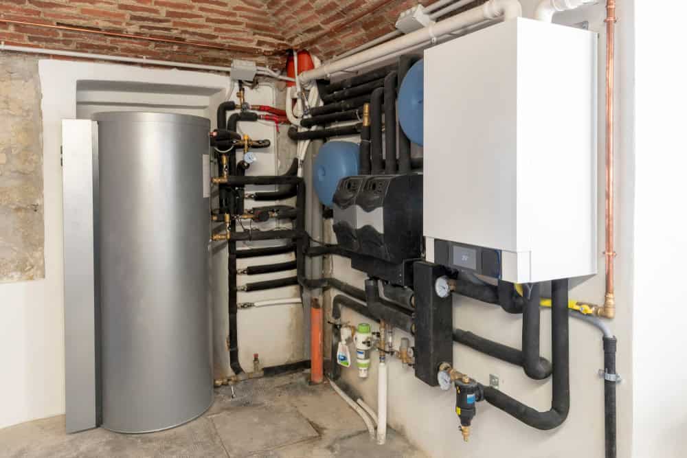 A utility room with a boiler, water heater, and various pipes and connections installed on the walls and ceiling, including propane services. The floor is concrete.